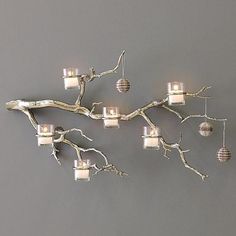 a branch with four lights hanging from it's sides on a gray wall in front of a grey background