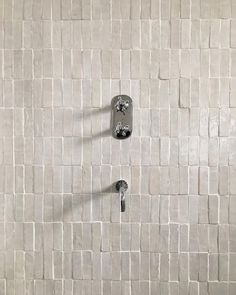 a white tiled wall with two faucets and one hand shower head in the middle