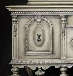 an ornate silver cabinet with two doors and one drawer on the top, in front of a black background