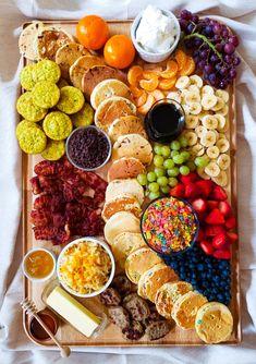 a wooden platter filled with different types of snacks and fruit on top of a white blanket