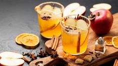 two glasses filled with apple cider on top of a cutting board