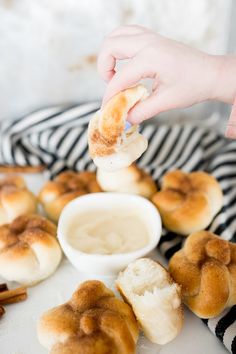 someone is dipping something in a small bowl with cinnamon buns on the table next to them