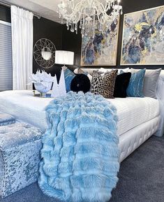 a bed with blue fur on it in a bedroom next to two paintings and a chandelier