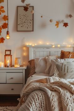 a bedroom with white furniture and fall leaves on the wall above the bed, along with candles