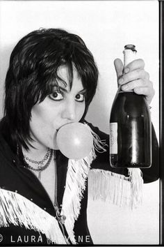 a woman holding a bottle and chewing on an apple in front of her face while wearing fringes