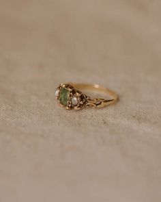 a gold ring with two green stones on the front and one stone in the back