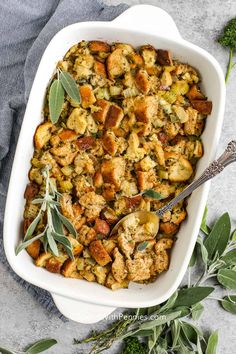 a casserole dish filled with stuffing and sage sprigs on the side