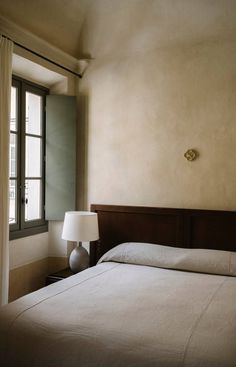 a bed sitting next to a window and a lamp on top of a wooden headboard