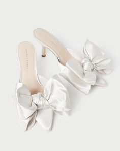 a pair of white high heeled shoes with a large bow on the front and side