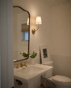 a white toilet sitting next to a sink under a bathroom mirror with flowers on it