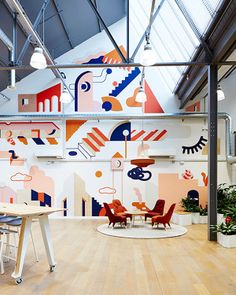 an office with colorfully painted walls and chairs in the foreground is a round table surrounded by stools