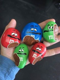 four rocks painted to look like m & m's are in the palm of someone's hand