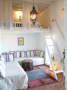 a living room with white couches and colorful rugs on the floor in front of a loft bed