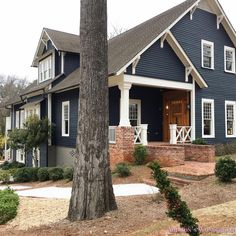 a blue house with white trim on the front door and porch, surrounded by trees