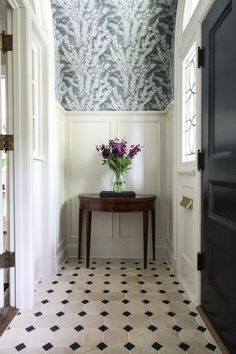 a vase with purple flowers sitting on top of a table in a hallway next to a doorway