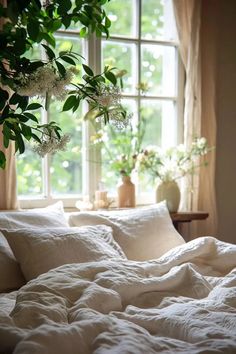 an unmade bed in front of a window with white sheets and pillows on it