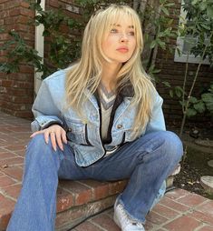 a blonde woman sitting on top of a brick wall next to a green planter