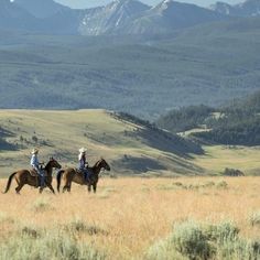 two people are riding horses in the mountains