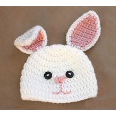 a crocheted bunny hat with black eyes and ears is shown on a brown surface