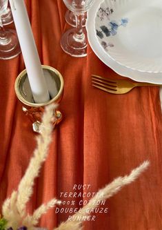 an orange table cloth with white plates and silverware on it, next to a gold candle holder