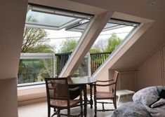 an attic bedroom with three large windows and a table in the corner between two beds