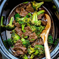 beef and broccoli in a slow cooker with a wooden spoon on the side