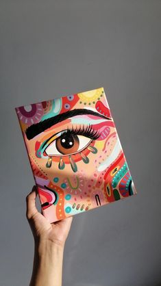 a hand holding up a colorful box with an eye painted on the front and side