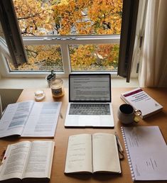 an open laptop computer sitting on top of a wooden desk next to books and papers