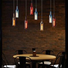 a dining room table with chairs and lights hanging from the ceiling above it, in front of a brick wall