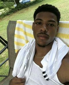 a man sitting in a chair with a towel around his neck and wearing a white tank top