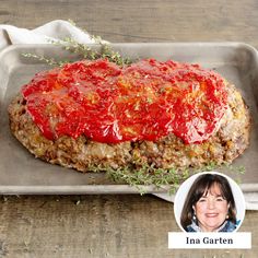 a large meatloaf covered in ketchup on a baking pan with a woman's face next to it