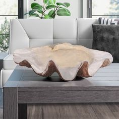 a table with a bowl on it in front of a couch and potted plant