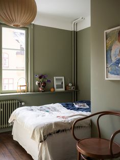 a bedroom with a bed, chair and painting on the wall in it's corner