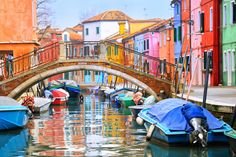 several boats are parked in the water near buildings and a bridge over which is painted with colorful colors