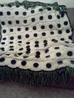 a crocheted blanket with black dots and green grass on it sitting on a couch