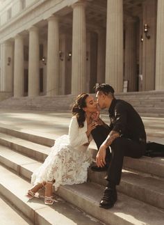 a man and woman sitting on steps in front of a building, kissing each other