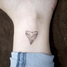 a small tattoo on the ankle of a woman's foot with a shark tooth