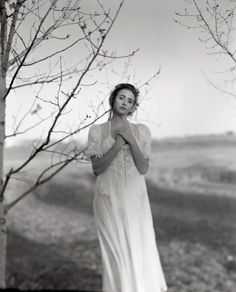 black and white photograph of a woman standing in front of a tree with her hands folded