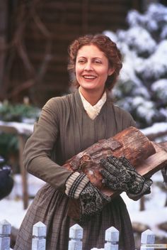 a woman holding a piece of wood in her right hand and smiling at the camera