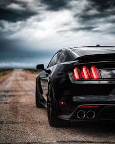 the rear end of a black sports car on a dirt road with dark clouds in the background