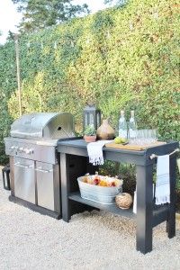 an outdoor bbq with grill and table next to it in the middle of some bushes