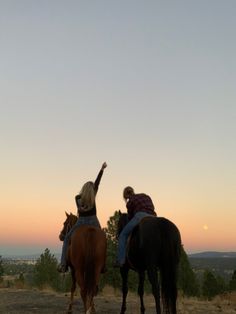 two people riding horses on a dirt road at sunset with the sky in the background