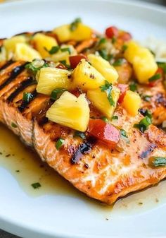 grilled salmon topped with pineapple salsa on a white plate, ready to be eaten