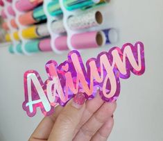 a person holding up a pink sticker with the word august spelled in large letters