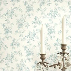 two white candles sitting on top of a chandelier in front of a floral wallpaper