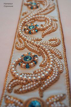 the beaded ribbon is decorated with pearls and blue stones on white fabric, as well as gold trimming