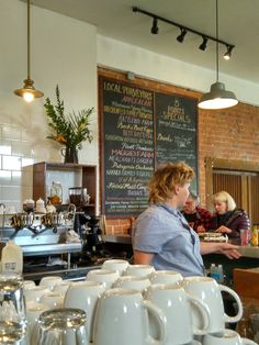 two women working behind the counter at a coffee shop with cups on display in front of them