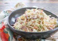 a black bowl filled with coleslaw on top of a colorful table cloth next to a wooden spoon