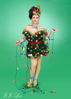 a woman in a green dress is dressed up as a christmas tree with lights on it