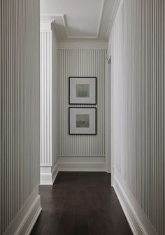 an empty hallway with two pictures hanging on the wall and wood flooring in front of it